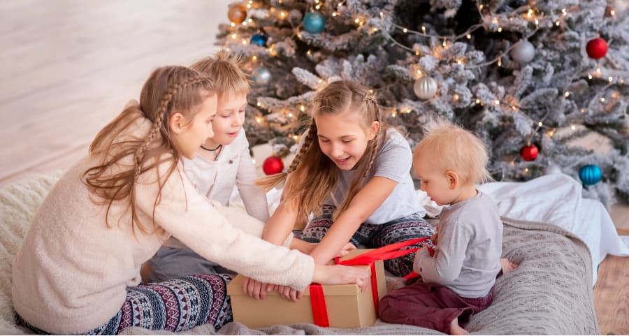 Siblings opening a gift beside a Christmas tree.